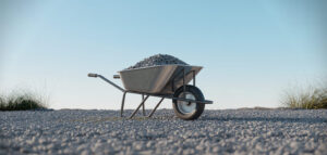 En ultra-minimalistisk bild av en skottkärra fylld med grus i ett soligt landskap.
