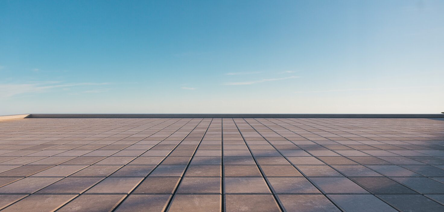 En minimalistisk uteplats med betongsten under en klarblå himmel, fokuserat på det rena utseendet och de raka linjerna.